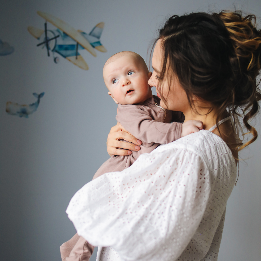 Mother holding her baby in a softly lit nursery, representing early oral health and baby tongue tie education for parents.