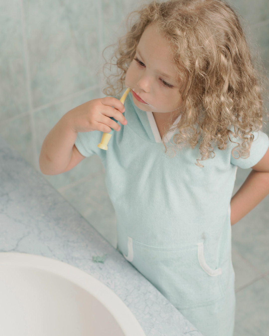Young child brushing teeth in the bathroom, illustrating parental support and the 7-year rule for kids learning oral hygiene independence.