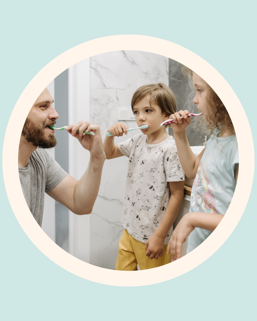 A father kneeling in a bathroom brushing his teeth alongside his two young children, modelling good oral hygiene habits, The Face Place children's dental health guide.