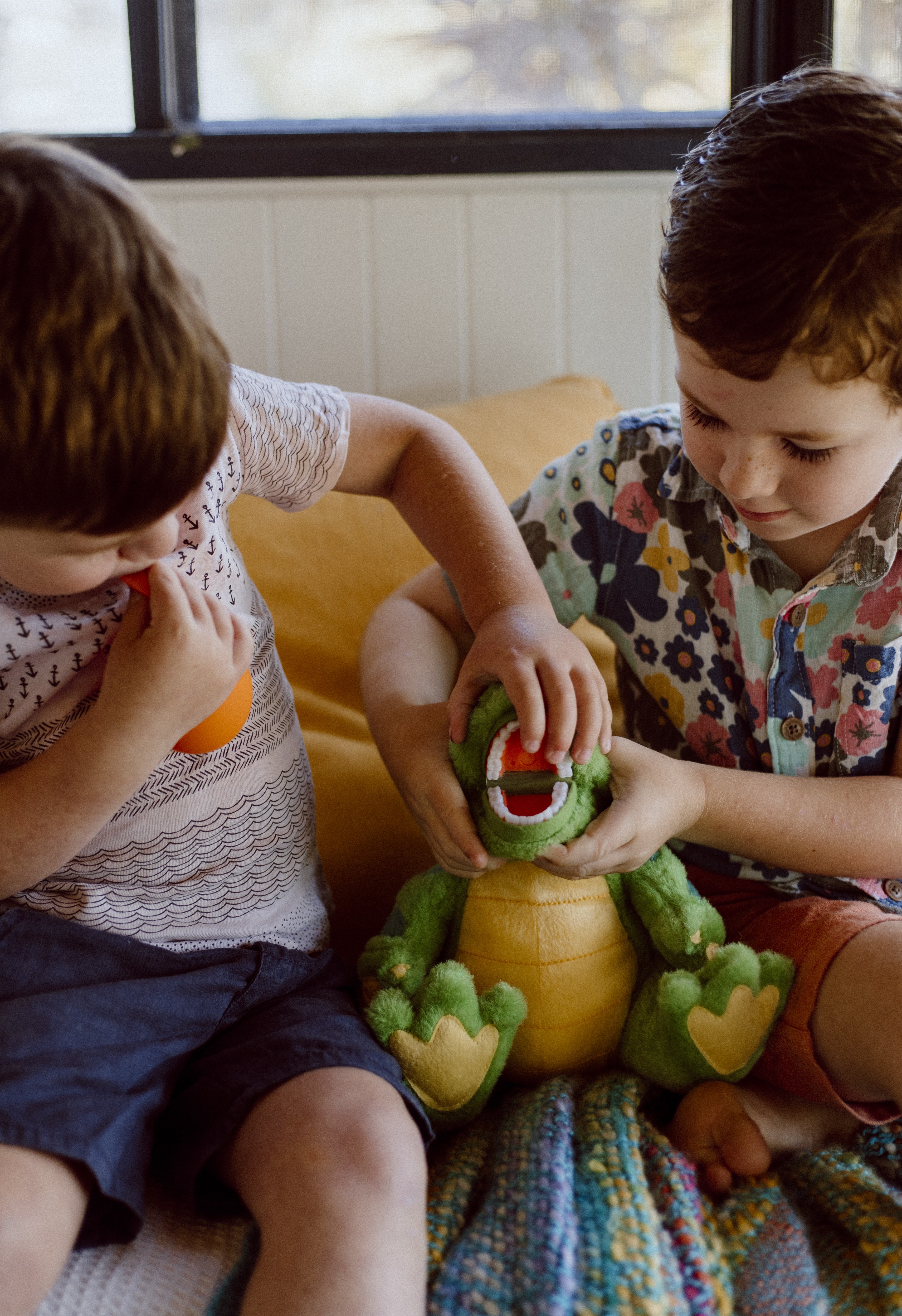A children’s oral health therapist smiling while delivering an online consultation on her laptop, seated at a wooden table with plants in the background.