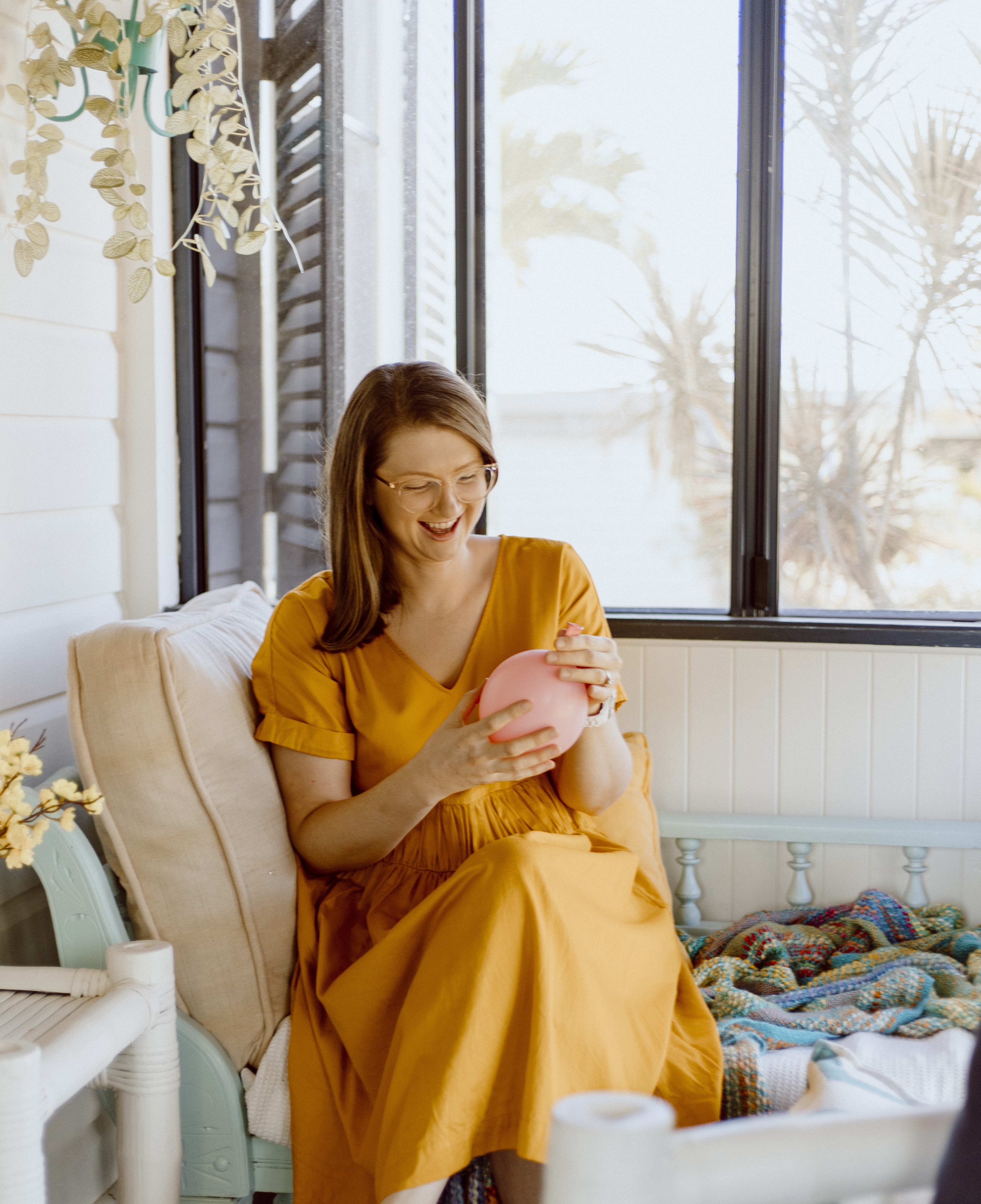 Oral health therapist Mel Van Schelven from The Face Place sitting by a sunny window, demonstrating a breathing exercise with a balloon to support children’s oral function and development.