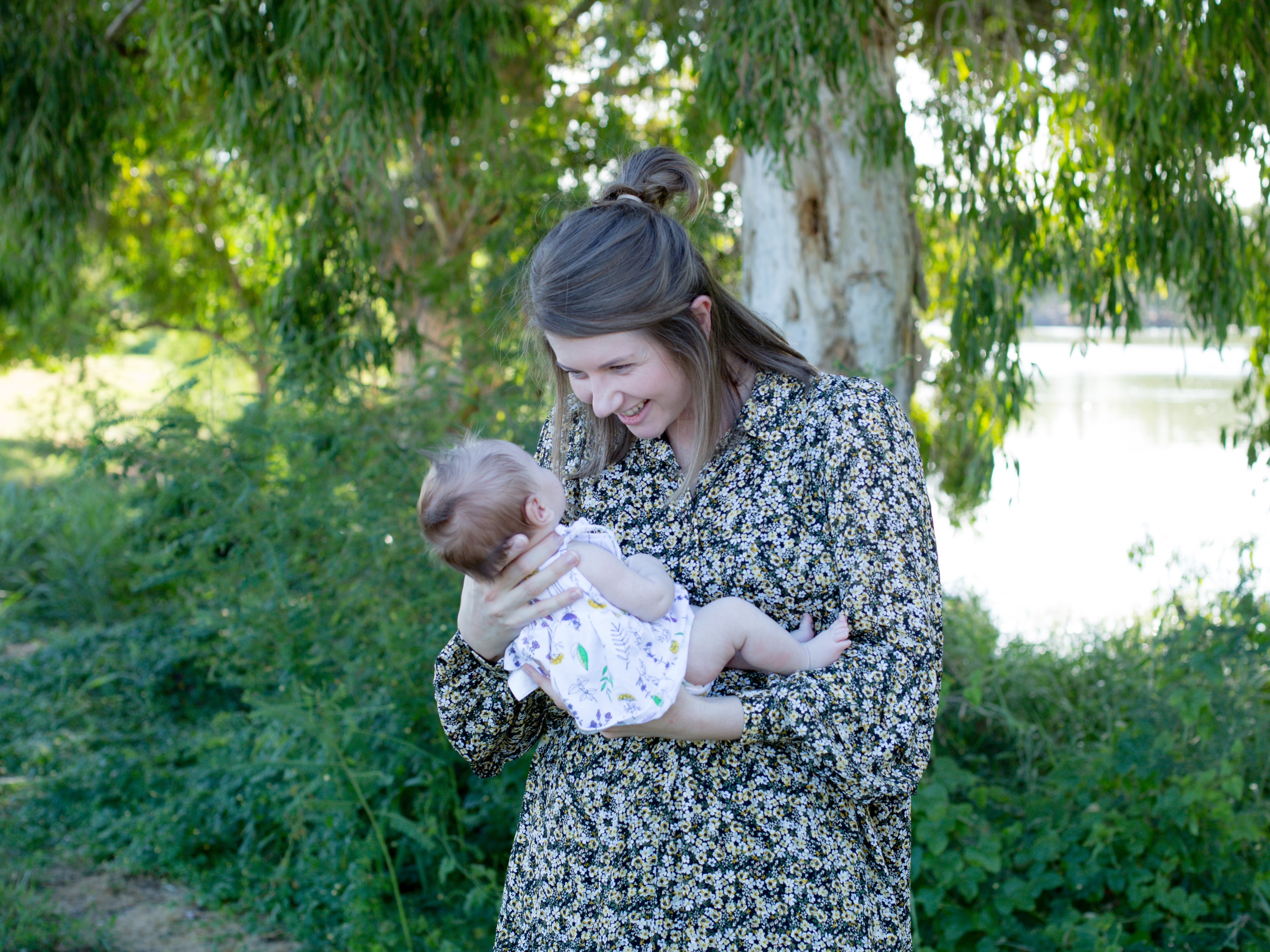 Smiling mother holding baby outdoors, symbolising bonding, early feeding and oral health education for parents learning about oral ties.