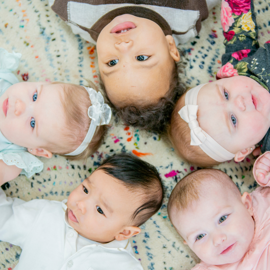 Group of babies lying on a patterned rug, representing infant development and oral ties awareness for parents learning about tongue and lip ties.