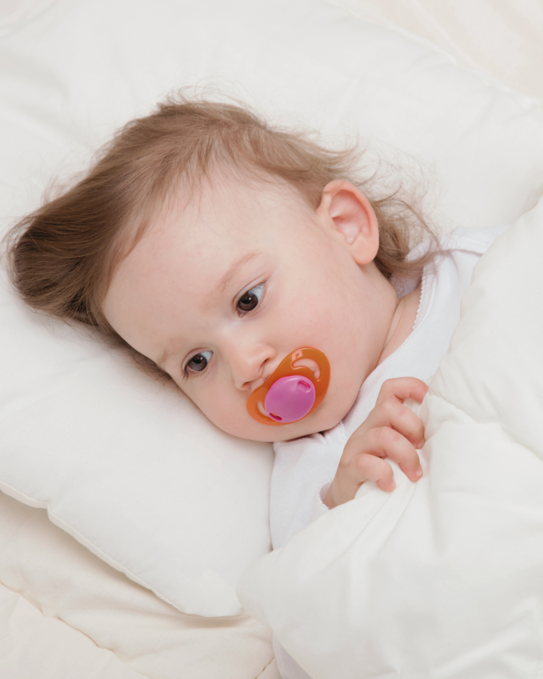 A young baby lying on a white pillow with a dummy, illustrating the topic of dummy use and dummy weaning for toddlers
