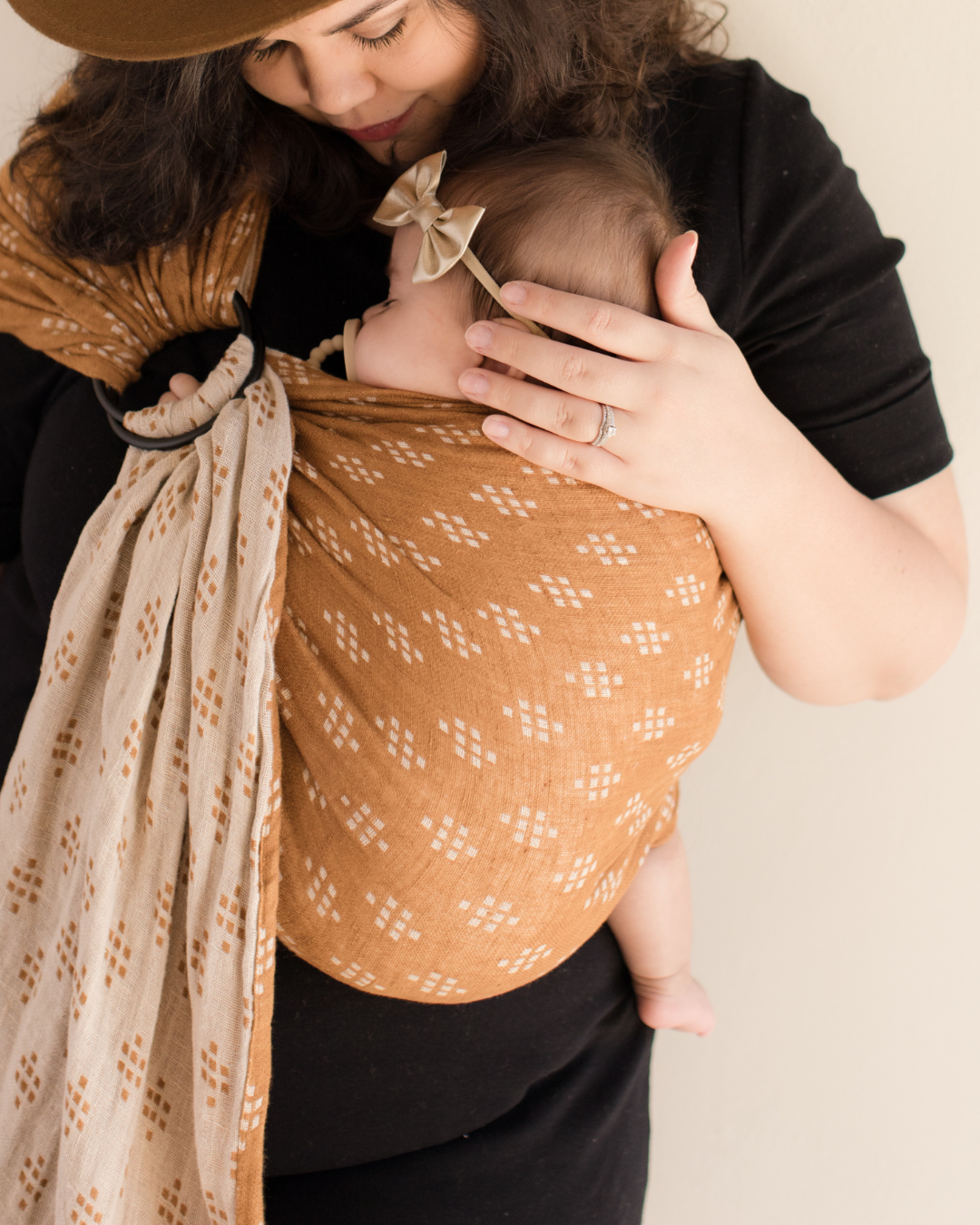 Mother holding baby in a brown sling, representing bonding, feeding support and oral ties education for parents of babies.
